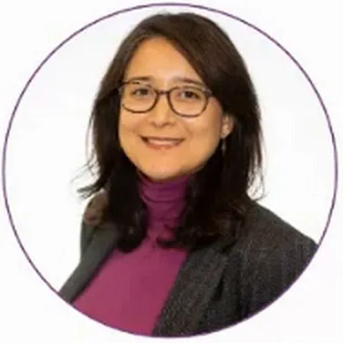 Jamile Tuma wearing glasses, a purple high-neck top and a dark jacket in her presentation portrait